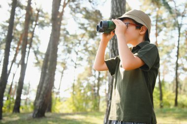 Little boy scout with binoculars during hiking in autumn forest. Concepts of adventure, scouting and hiking tourism for kids