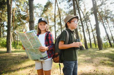 Two happy children having fun during forest hike on beautiful day in pine forest. Cute boy scout with binoculars during hiking in summer forest. Concepts of adventure, scouting and hiking tourism.