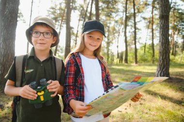 Two happy children having fun during forest hike on beautiful day in pine forest. Cute boy scout with binoculars during hiking in summer forest. Concepts of adventure, scouting and hiking tourism.