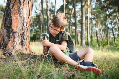 schoolboy is exploring nature with magnifying glass. Summer vacation for inquisitive kids in forest. Hiking. Boy-scout