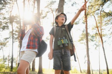 Happy excited school children with backpacks in casual clothes enjoying walk in forest on sunny autumn day, two active kids boy and girl running and playing together during camping trip in nature