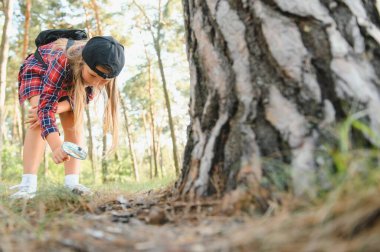 Sevimli küçük kız arka görüş görüntüsü büyüteç açık doğa keşfetmek. Büyüteçle ormanda oynayan çocuk. Meraklı çocuk parktaki ağaca büyüteçle bakıyor