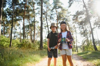 boy and girl go hiking with backpacks on forest road bright sunny day.
