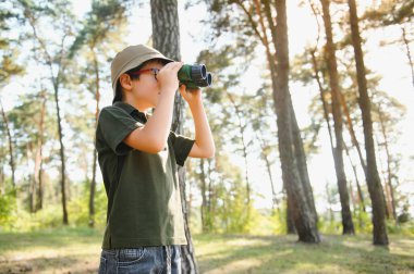 Boy with binoculars. Kid in green forest at summer daytime together