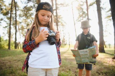 Group of curious happy school kids in casual clothes with backpacks exploring nature and forest together on sunny autumn day