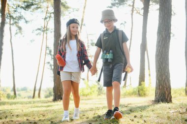 boy and girl go hiking with backpacks on forest road bright sunny day.