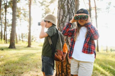 boy and girl go hiking with backpacks on forest road bright sunny day.