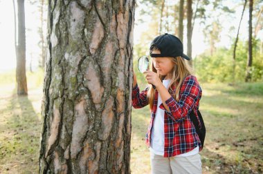 Sevimli küçük kız arka görüş görüntüsü büyüteç açık doğa keşfetmek. Büyüteçle ormanda oynayan çocuk. Meraklı çocuk parktaki ağaca büyüteçle bakıyor