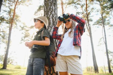 Happy excited school children with backpacks in casual clothes enjoying walk in forest on sunny autumn day, two active kids boy and girl running and playing together during camping trip in nature