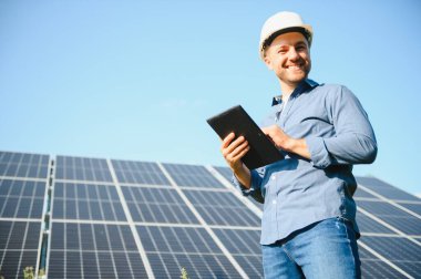 The portrait of a young engineer checks with tablet operation with sun, cleanliness on field of photovoltaic solar panels. Concept: renewable energy, technology, electricity, service, green power.