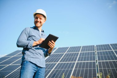 The portrait of a young engineer checks with tablet operation with sun, cleanliness on field of photovoltaic solar panels. Concept: renewable energy, technology, electricity, service, green power.