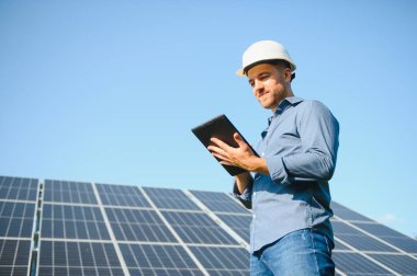 The portrait of a young engineer checks with tablet operation with sun, cleanliness on field of photovoltaic solar panels. Concept: renewable energy, technology, electricity, service, green power.
