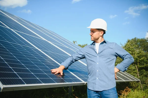 Male engineer in a helmet standing near the solar panels, looking up. Green ecological power energy generation. Solar station development concept. Home construction