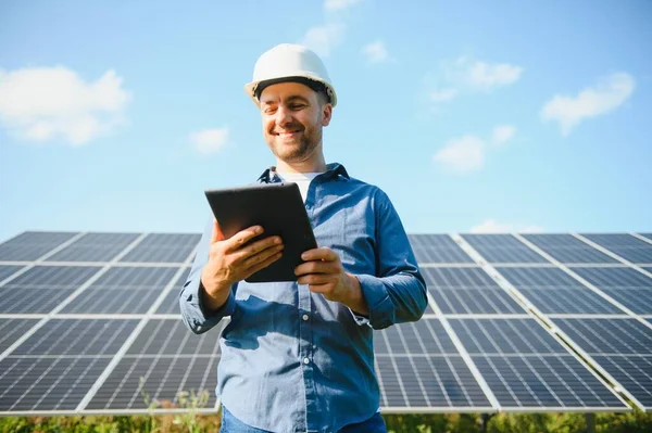 The portrait of a young engineer checks with tablet operation with sun, cleanliness on field of photovoltaic solar panels. Concept: renewable energy, technology, electricity, service, green power.