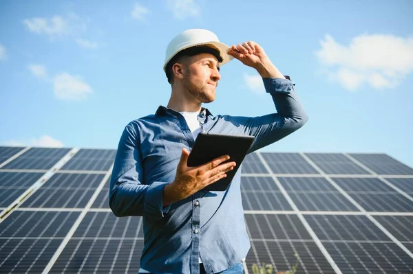 The portrait of a young engineer checks with tablet operation with sun, cleanliness on field of photovoltaic solar panels. Concept: renewable energy, technology, electricity, service, green power.