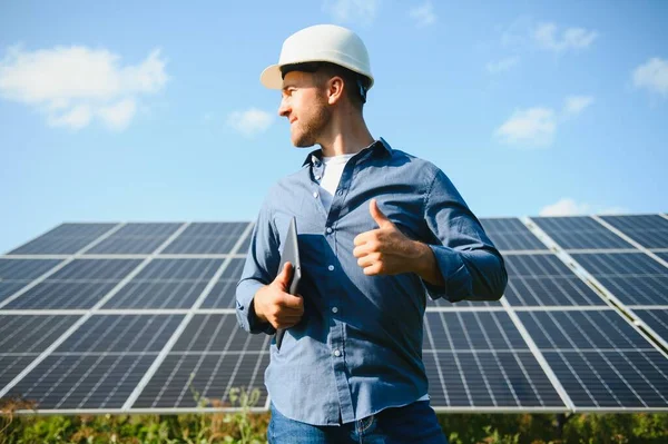 The portrait of a young engineer checks with tablet operation with sun, cleanliness on field of photovoltaic solar panels. Concept: renewable energy, technology, electricity, service, green power.