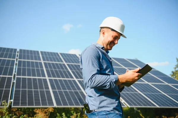 The portrait of a young engineer checks with tablet operation with sun, cleanliness on field of photovoltaic solar panels. Concept: renewable energy, technology, electricity, service, green power.