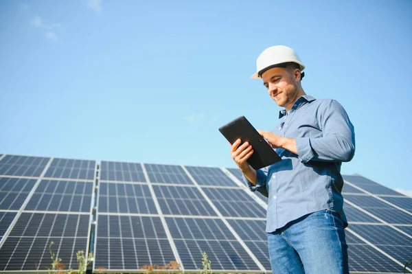 The portrait of a young engineer checks with tablet operation with sun, cleanliness on field of photovoltaic solar panels. Concept: renewable energy, technology, electricity, service, green power.