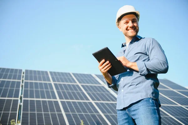 The portrait of a young engineer checks with tablet operation with sun, cleanliness on field of photovoltaic solar panels. Concept: renewable energy, technology, electricity, service, green power.
