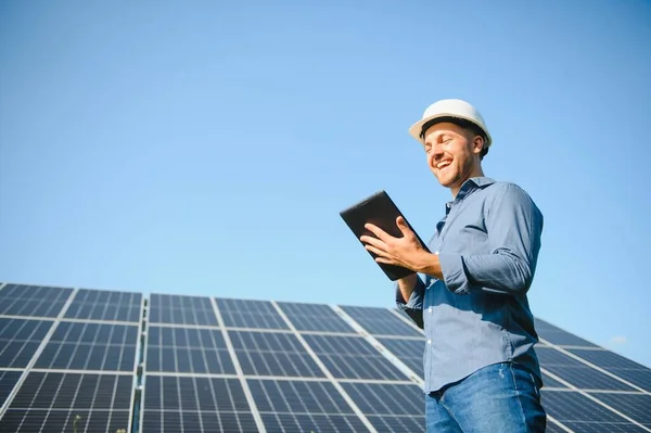 The portrait of a young engineer checks with tablet operation with sun, cleanliness on field of photovoltaic solar panels. Concept: renewable energy, technology, electricity, service, green power.