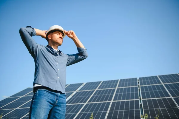 Male engineer in a helmet standing near the solar panels, looking up. Green ecological power energy generation. Solar station development concept. Home construction