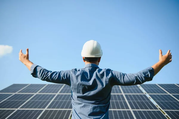 Happy working solar station raising his hands on a background of photovoltaic panels. Science solar energy.