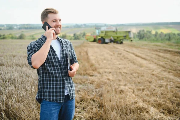 Handsome farmer with tablet standing in front of combine harvester during harvest in field