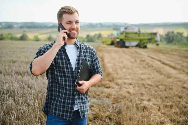 Handsome farmer with tablet standing in front of combine harvester during harvest in field