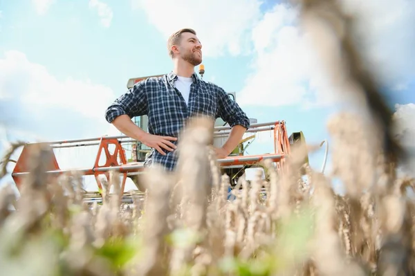 Handsome farmer with tablet standing in front of combine harvester during harvest in field