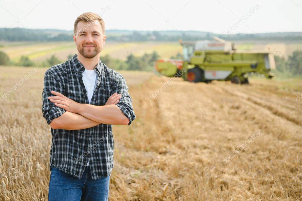 Happy farmer proudly standing in a field. Combine harvester driver going to crop rich wheat harvest. Agronomist wearing flannel shirt, looking at camera on a farmland.