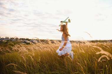 Happy kid with toy plane is playing at sunset.