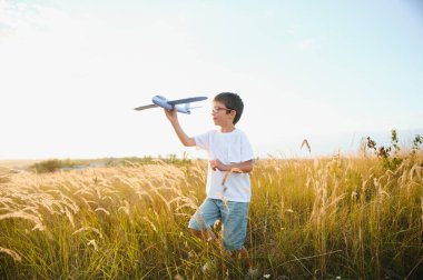 Cute happy cheerful child running fastly along grassy hill at countryside holding big toy plane in hand. Boy playing during sunset time in evening. Horizontal color photography
