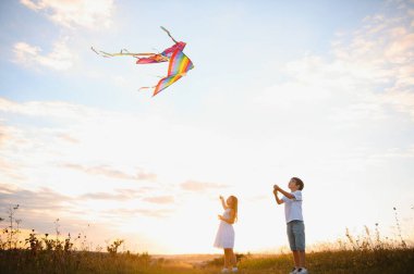 Çocuklar gün batımında sahada uçurtma fırlatırlar..
