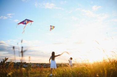 Happy boy and girl playing with kites in field at sunset. Happy childhood concept