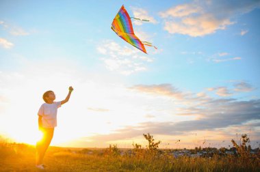 Çocuklar gün batımında sahada uçurtma fırlatırlar.