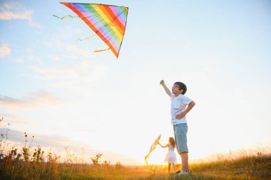 Çocuklar gün batımında sahada uçurtma fırlatırlar..