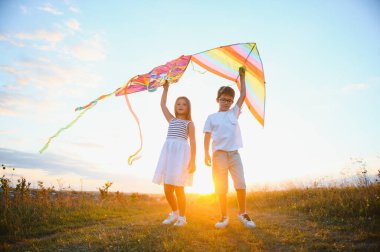 Çocuklar gün batımında sahada uçurtma fırlatırlar..
