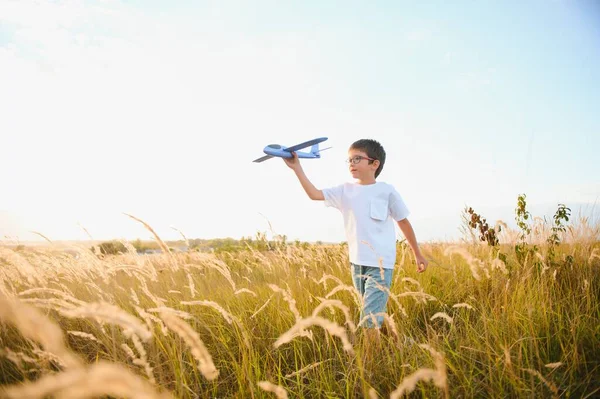 The kid runs with a toy plane. Son dreams of flying. Happy child, boy, runs on the sun playing with a toy airplane on the summer field.