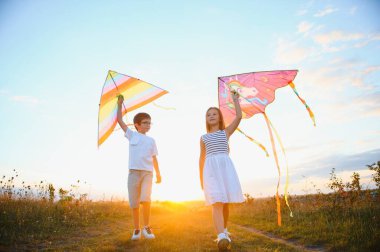 Happy boy and girl playing with kites in field at sunset. Happy childhood concept