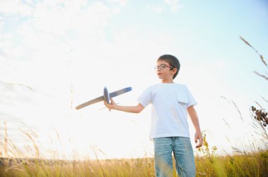 The kid runs with a toy plane. Son dreams of flying. Happy child, boy, runs on the sun playing with a toy airplane on the summer field.