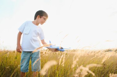 The kid runs with a toy plane. Son dreams of flying. Happy child, boy, runs on the sun playing with a toy airplane on the summer field.