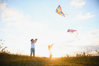 Çocuklar gün batımında sahada uçurtma fırlatırlar..
