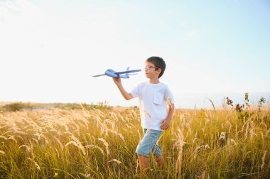 The kid runs with a toy plane. Son dreams of flying. Happy child, boy, runs on the sun playing with a toy airplane on the summer field.