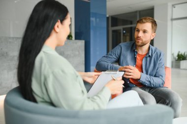 Psychologist talking with patient on therapy session. Depressed man speaking to a therapist while she is taking notes