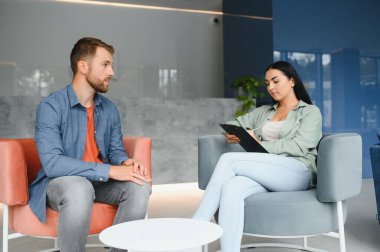 İş kavramı. Olgun neşeli ofis Müdürü önünde iş üzerinde oturan genç esmer kadın röportaj, onu deneyimi hakkında konuşmak rahatlatıcı sahip ve derecesi