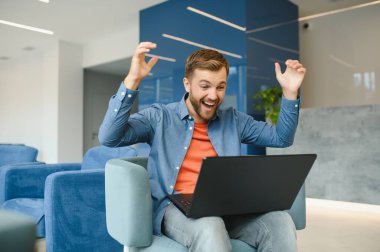 happy smiling remote online working man in casual outfit with laptop in joyful successful winning gesture sitting in an coworking office at a work desk