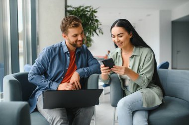 Smiling businesspeople work collaborate on computer, brainstorm over company startup at office meeting. Motivated diverse colleagues look at laptop screen discuss business project ideas together.