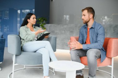 Psychologist talking with patient on therapy session. Depressed man speaking to a therapist while she is taking notes