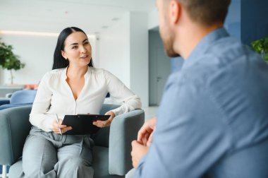 İş kavramı. Olgun neşeli ofis Müdürü önünde iş üzerinde oturan genç esmer kadın röportaj, onu deneyimi hakkında konuşmak rahatlatıcı sahip ve derecesi