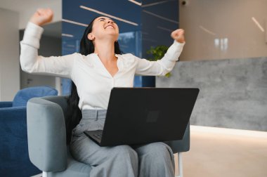 Portrait of excited young caucasian woman celebrating success while sitting with laptop at home or modern office Happy female freelancer working in coworking space.